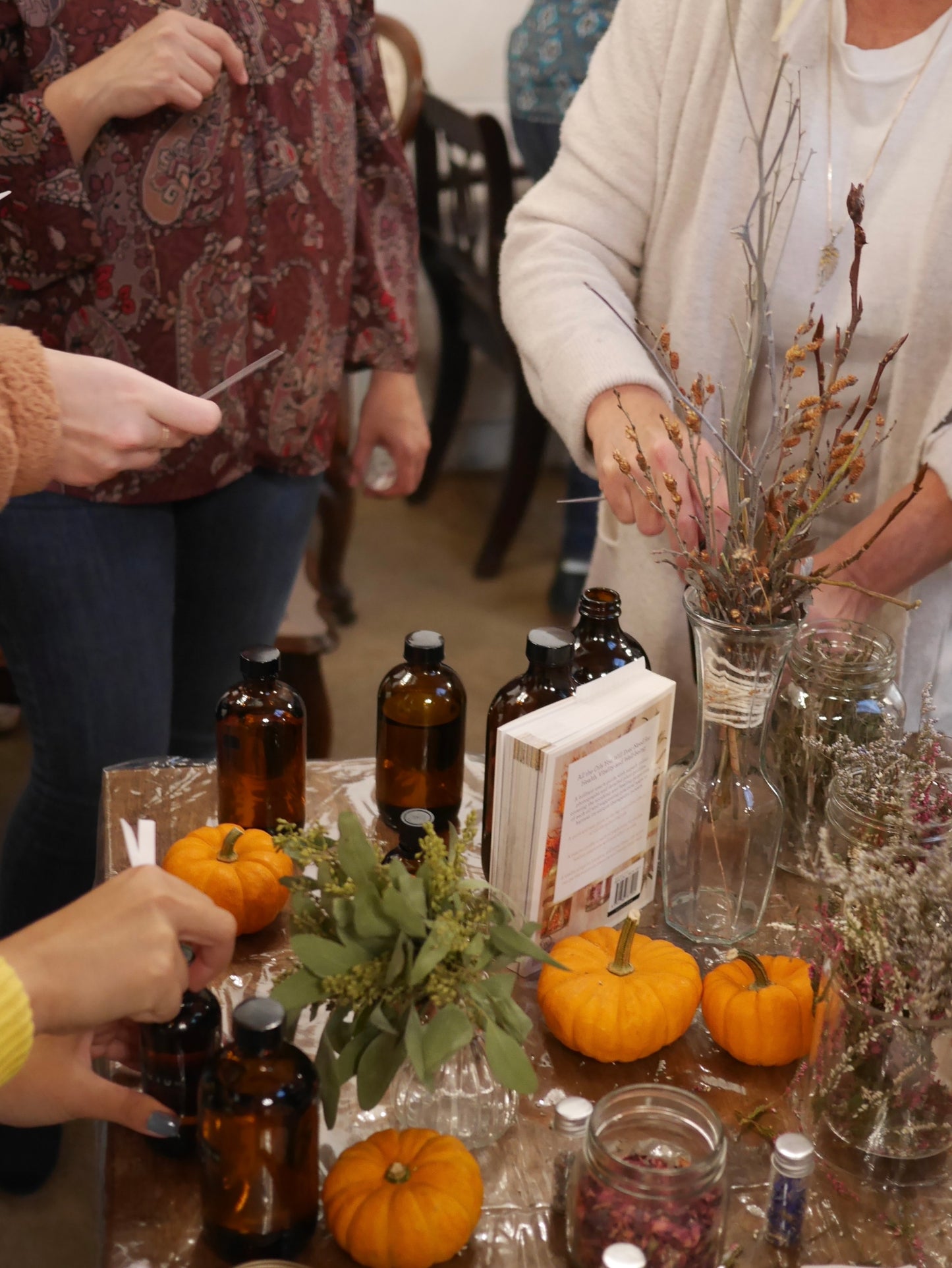 Group of women smelling scents from amber glass bottles and pumpkin fall foliage
