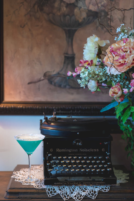 typewriter with a blue cocktail and floral arrangement on a desk
